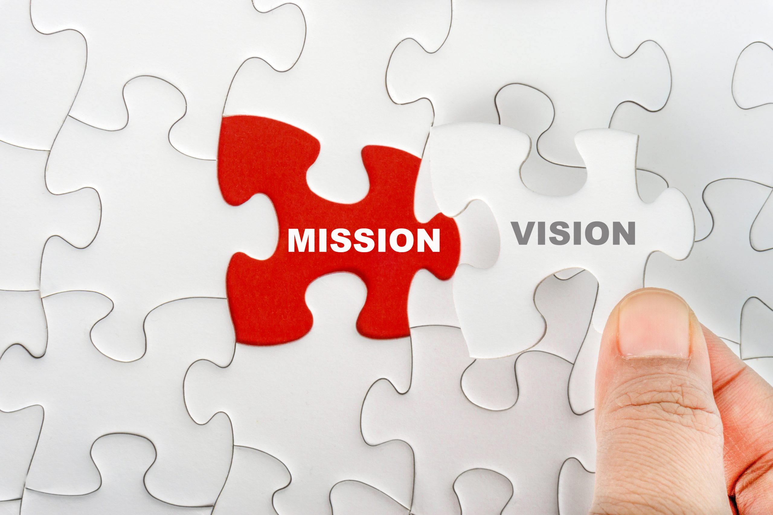 Hand holding piece of jigsaw puzzle with word MISSION VISION. Selective focus